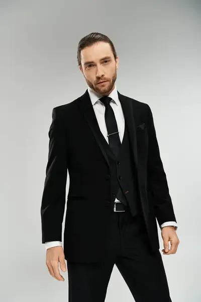 A bearded businessman exudes confidence and elegance as he poses in a suit and tie against a grey studio backdrop. — Stock Photo