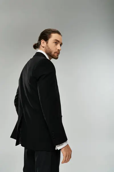 Стильний бородатий бізнесмен у костюмі впевнено стоїть на сірому фоні в обстановці студії. — стокове фото