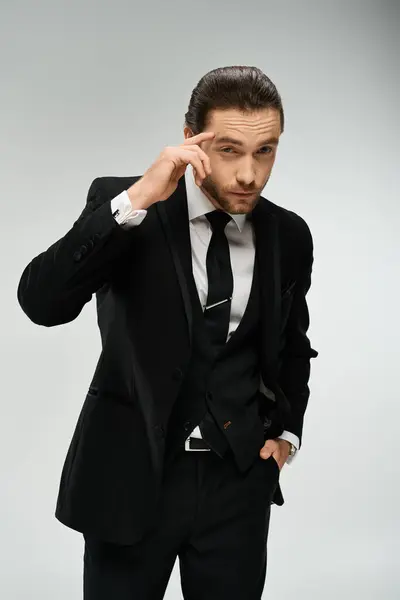 A handsome, bearded businessman in a suit holds his hand to his ear, listening intently. Studio shot on a grey background. — Stock Photo