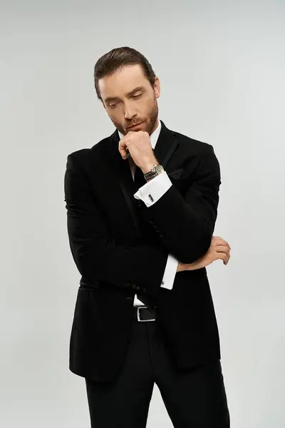A handsome, bearded businessman in a tuxedo poses confidently for the camera in a studio setting on a grey background. — Stock Photo