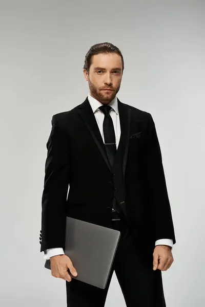 A bearded businessman in a sharp suit confidently holds a laptop in a sleek, professional studio setting. — Stock Photo