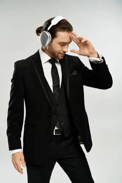 A bearded, handsome businessman in a suit listening to music with headphones in a studio on a grey background. — Stock Photo