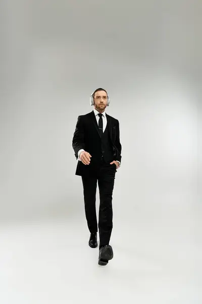 A handsome, bearded businessman in a suit and tie walks confidently in a studio against a grey background. — Stock Photo