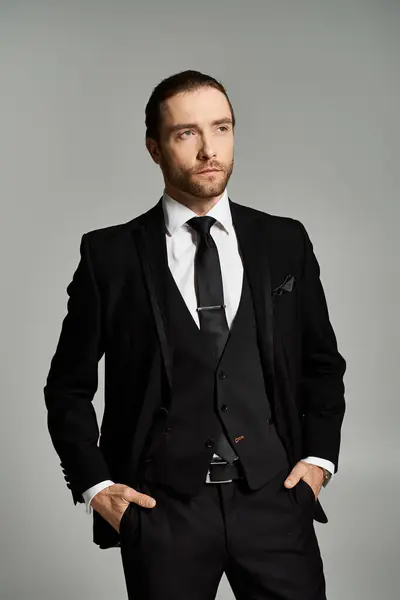 Ein bärtiger und gutaussehender Geschäftsmann posiert selbstbewusst in Anzug und Krawatte vor grauer Studiokulisse. — Stockfoto