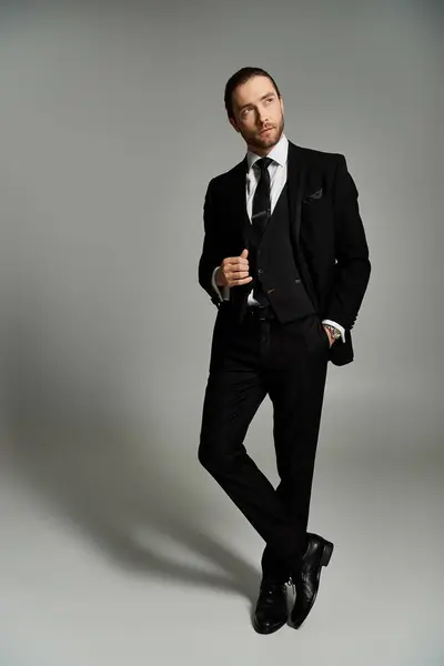 A handsome, bearded businessman confidently poses in a stylish tuxedo against a grey studio background. — Stock Photo