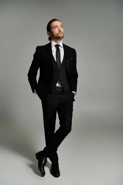 Um empresário bonito e barbudo de terno e gravata marcando uma pose confiante em um fundo de estúdio cinza. — Fotografia de Stock