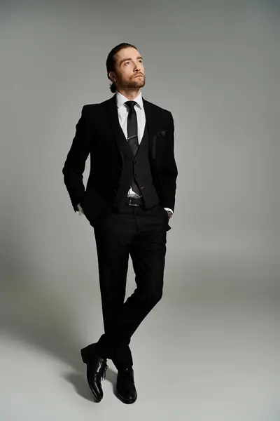 A handsome and bearded businessman in a suit and tie striking a confident pose on a grey studio background. — Stock Photo