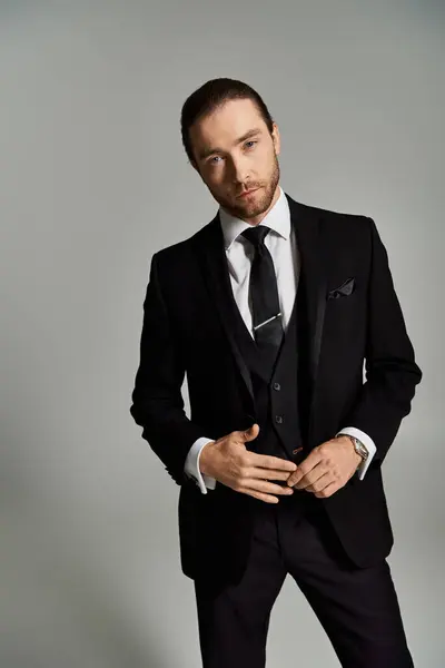 Un gentleman élégant en costume et cravate pose en toute confiance pour un portrait en studio sur fond gris. — Photo de stock