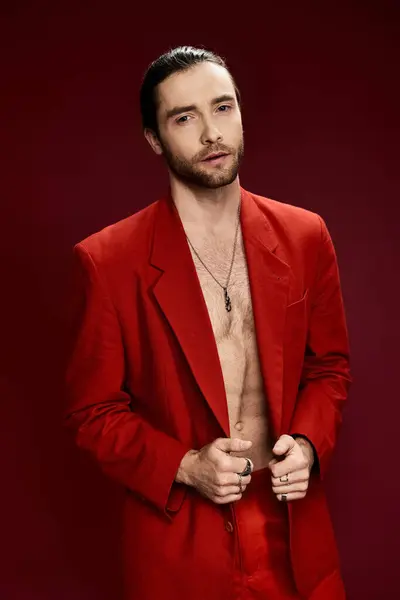 Um homem bonito em um terno vermelho elegante golpeia uma pose confiante sem uma camisa sobre em um ajuste do estúdio. — Fotografia de Stock