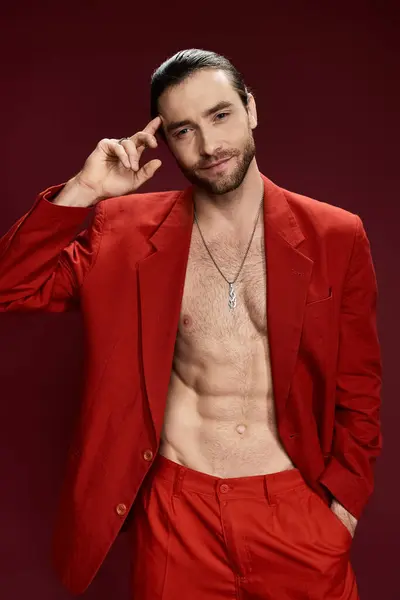 Un bel homme en costume rouge frappant, torse nu, posant en toute confiance dans un décor de studio. — Photo de stock