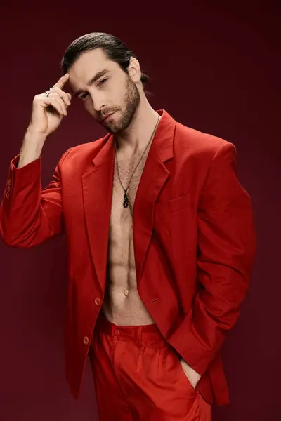 Ein gutaussehender Mann posiert selbstbewusst in einem auffallend roten Anzug ohne Hemd in einem professionellen Studio-Setting. — Stockfoto
