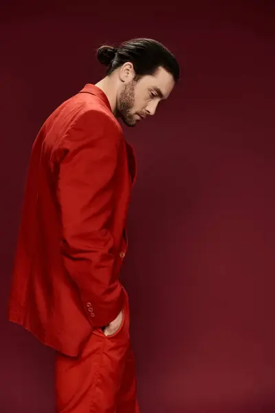 Красивий чоловік у червоному костюмі, без сорочки, вражає потужну позу перед яскравою червоною стіною. — стокове фото