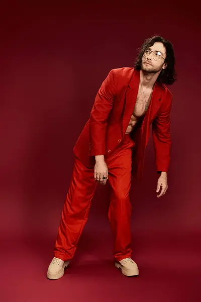 Un homme habillé d'un costume rouge saisissant pose avec confiance alors qu'il est torse nu dans un décor de studio. — Photo de stock