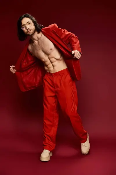 Un bel homme en costume rouge vibrant pose en toute confiance dans un studio sans chemise. — Photo de stock