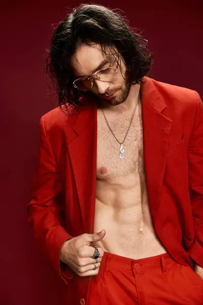 Handsome man confidently poses in a red suit without a shirt in a stylish studio setting. — Stock Photo