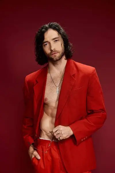 Homem bonito em um terno vermelho impressionante, sem camisa, marcando uma pose confiante em um ambiente de estúdio. — Fotografia de Stock