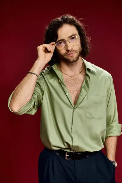 Ein gutaussehender Mann mit Brille und grünem Seidenhemd posiert vor leuchtend rotem Hintergrund. — Stockfoto
