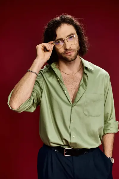 A handsome man in glasses and a green silk shirt striking a pose on a vibrant red background. — Stock Photo