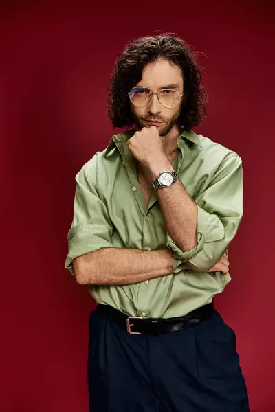 Красивий чоловік в окулярах і зелена шовкова сорочка демонструє розкішний годинник на лівій руці на сміливому червоному тлі. — стокове фото