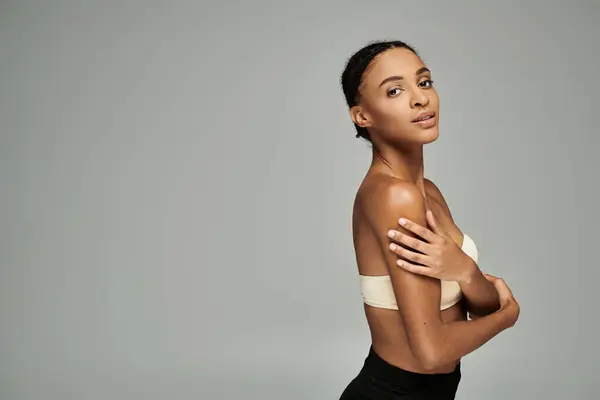 Young African American woman in a strapless top, crossing her arms confidently on a grey background. — Stock Photo