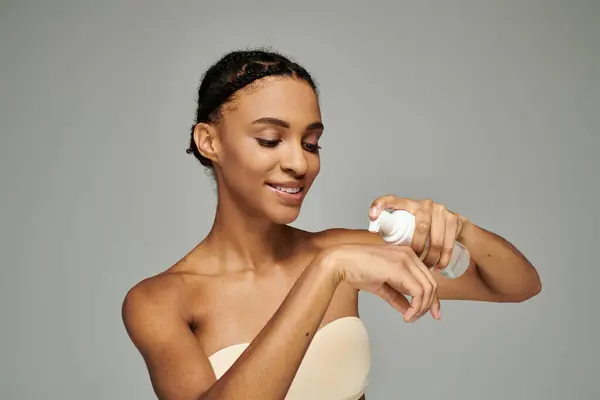 Young African American woman in a strapless dress holding a bottle of facial cleanser, taking care of her skin. — Stock Photo