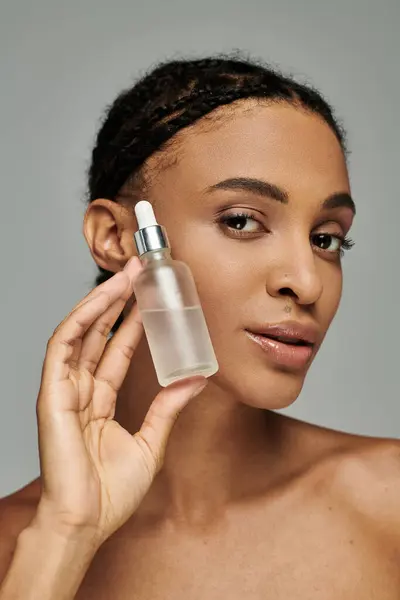 Beautiful young African American woman in strapless top holding serum to her face with focused care. — Stock Photo