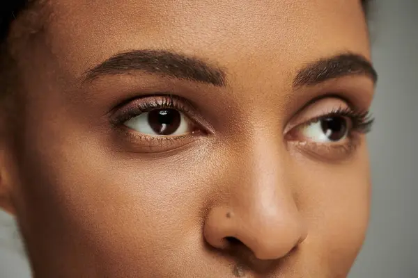 Nahaufnahme einer jungen Afroamerikanerin mit atemberaubenden braunen Augen, Hautpflege-Routine auf grauem Hintergrund. — Stockfoto