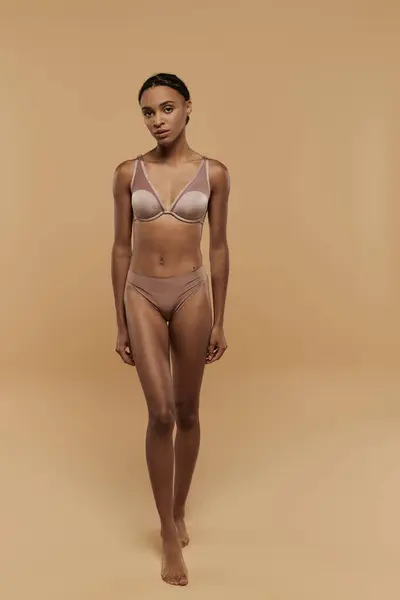 Pretty, slim African American woman stands confidently in a bikini against a beige backdrop, radiating self-care and beauty. — Stock Photo