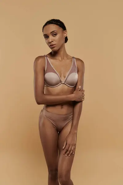 A pretty and slim African American woman is pampering herself in a tan bra and panties on a beige background. — Stock Photo