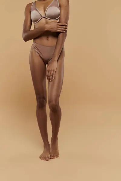 Uma mulher afro-americana deslumbrante em um biquíni faz uma pose graciosa contra um pano de fundo bege. — Fotografia de Stock