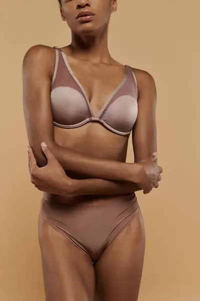 African American woman in bra and panties poses gracefully against a beige backdrop, showcasing her confidence and body care routine. — Stock Photo