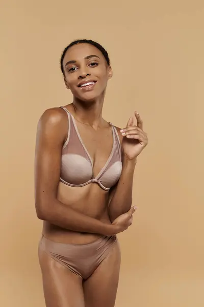 Una splendida donna afroamericana snella e slanciata posa elegantemente in un reggiseno nudo, trasudando fiducia e sicurezza in se stessi su un morbido sfondo beige. — Foto stock