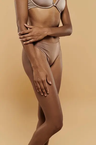 Mulher afro-americana em sutiã bronzeado e calcinha mostra auto-cuidado em um fundo bege. — Fotografia de Stock