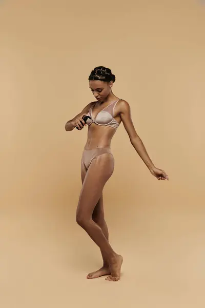 Schöne, schlanke Afroamerikanerin steht selbstbewusst im Bikini vor beigem Hintergrund. — Stockfoto