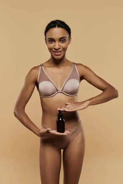 Une femme afro-américaine mince en bikini tenant une bouteille d'huile corporelle, exsudant dynamisme et détente sur une plage ensoleillée. — Photo de stock