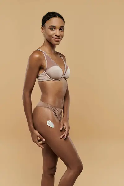 Bella, sottile donna afroamericana posa con fiducia in bikini su sfondo beige. — Foto stock
