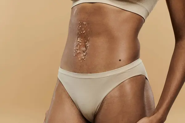Uno squisito pezzo di pelle posto sullo stomaco di una donna afroamericana magra in biancheria intima. — Foto stock