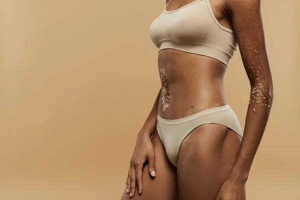 Donna afroamericana in bikini che colpisce una posa su sfondo beige. — Foto stock