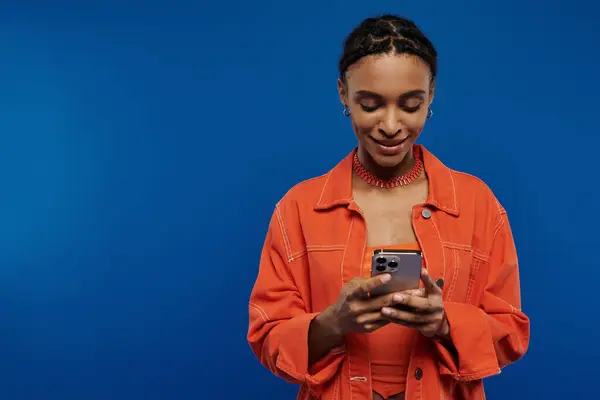A young African American woman in an orange shirt is focused on her cellphone. — Stock Photo