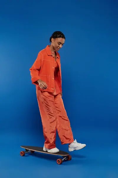 A woman in an orange jumpsuit effortlessly rides a skateboard, showcasing skills and freedom of movement. — Stock Photo