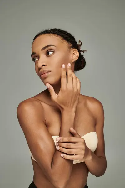 Young African American woman in a bra, exuding confidence and self-care on a grey background. — Stock Photo