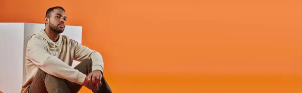 Стильный афроамериканец, сидящий на оранжевом фоне. — стоковое фото