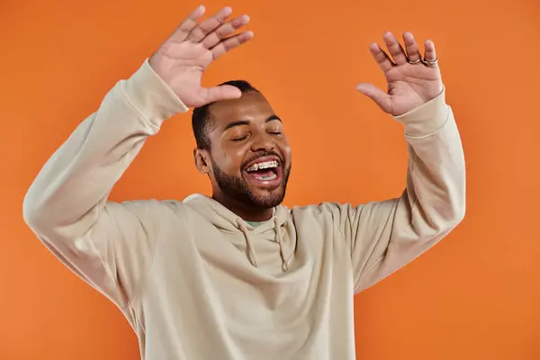 A stylish African American man with hands raised in delight on a vibrant backdrop. — Stock Photo