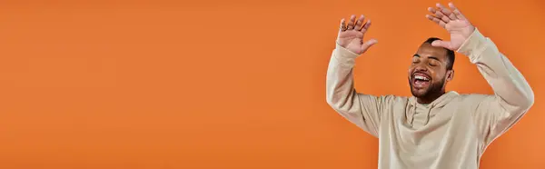A stylish African American man joyfully raises his hands against a vibrant backdrop. — Stock Photo