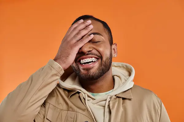 African American man in distress with hands on face against vibrant backdrop. — Stock Photo
