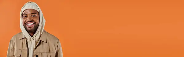 Ein stylischer afroamerikanischer Mann im Kapuzenpulli posiert selbstbewusst vor einem leuchtend orangefarbenen Hintergrund. — Stockfoto