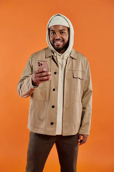 African American man in tan jacket engages with cell phone. — Stock Photo