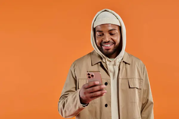 African American man in hoodie absorbed by smartphone, colorful background. — Stock Photo