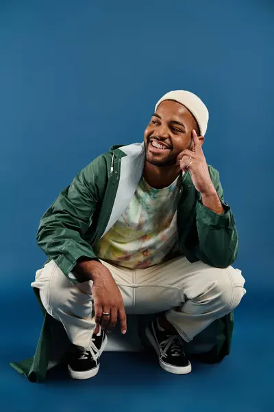An African American man in stylish attire sits on the ground, hand to his face deep in thought. — Stock Photo