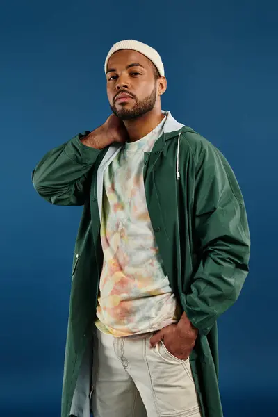 A stylish African American man in a green jacket and white hat poses against a vibrant backdrop. — Stock Photo